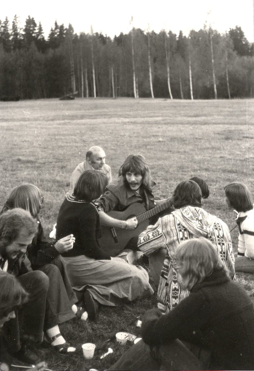 Personer, en med gitarr, på en gräsmatta med en björkskog bakom..