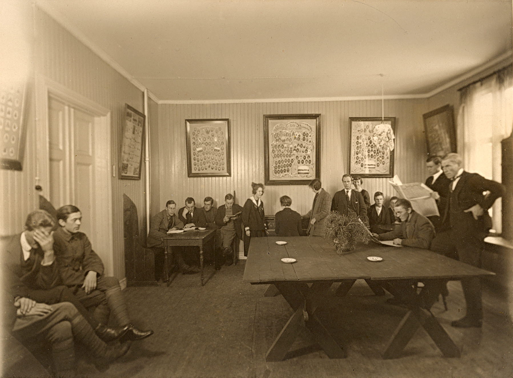 Personer i ett gammeldags sällskapsrum med trämöbler och stora tavlor på väggarna.