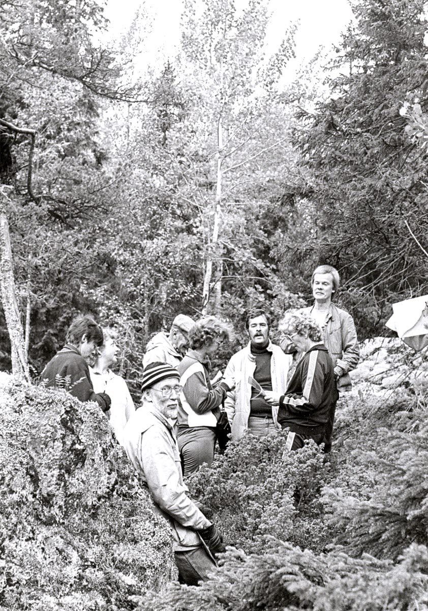 Personer klädda i träningsoveraller i en skogsdunge med en stor sten. 
