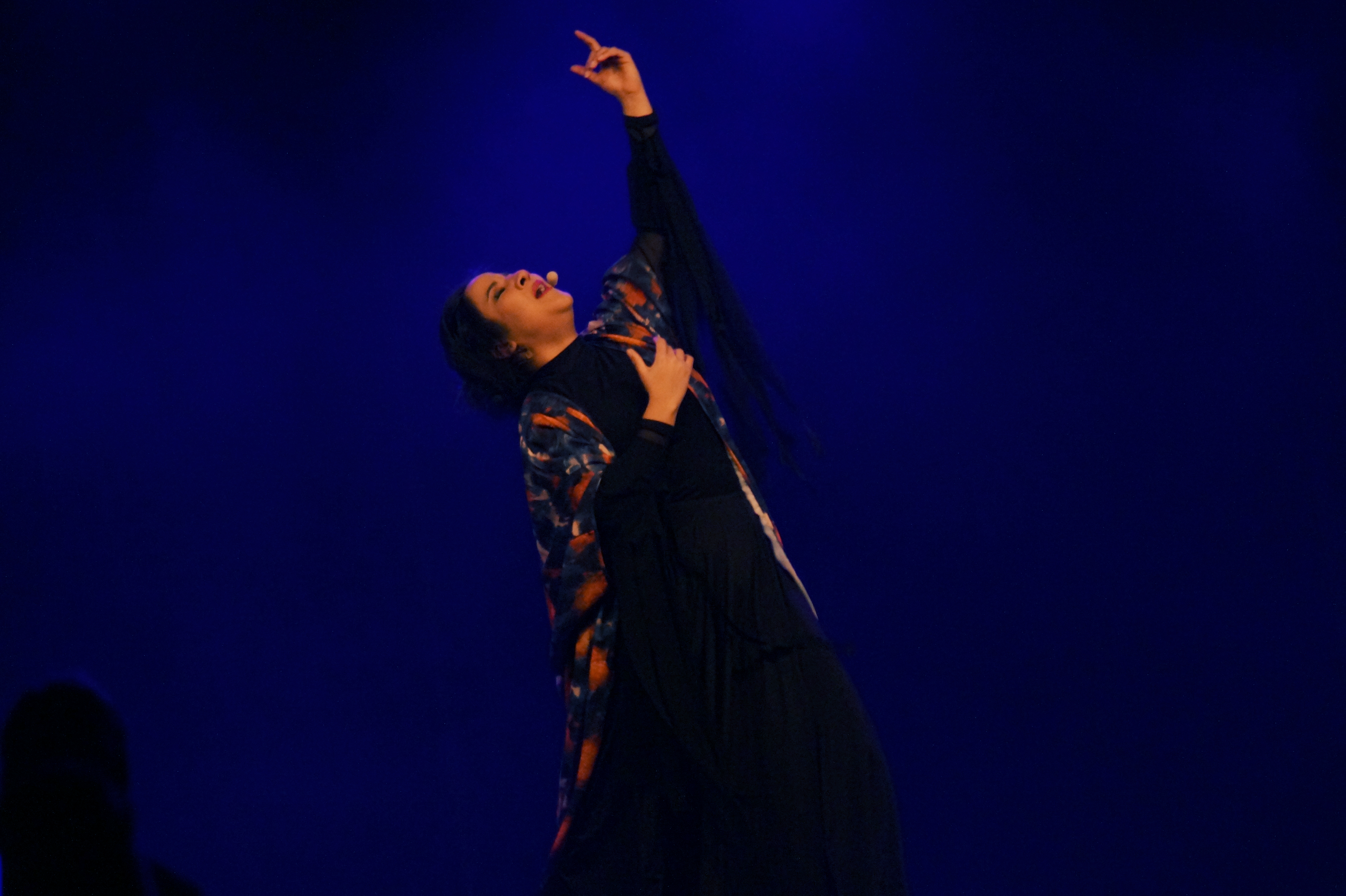 En kvinna står i dramatisk pose  på en scen och sjunger